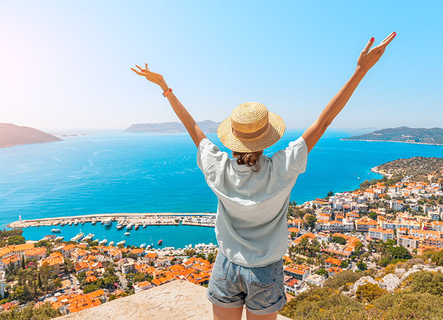 Happy woman with open arms stands on the viewpoint and enjoys the panorama of Kas resort town of the Mediterranean sea in Turkey