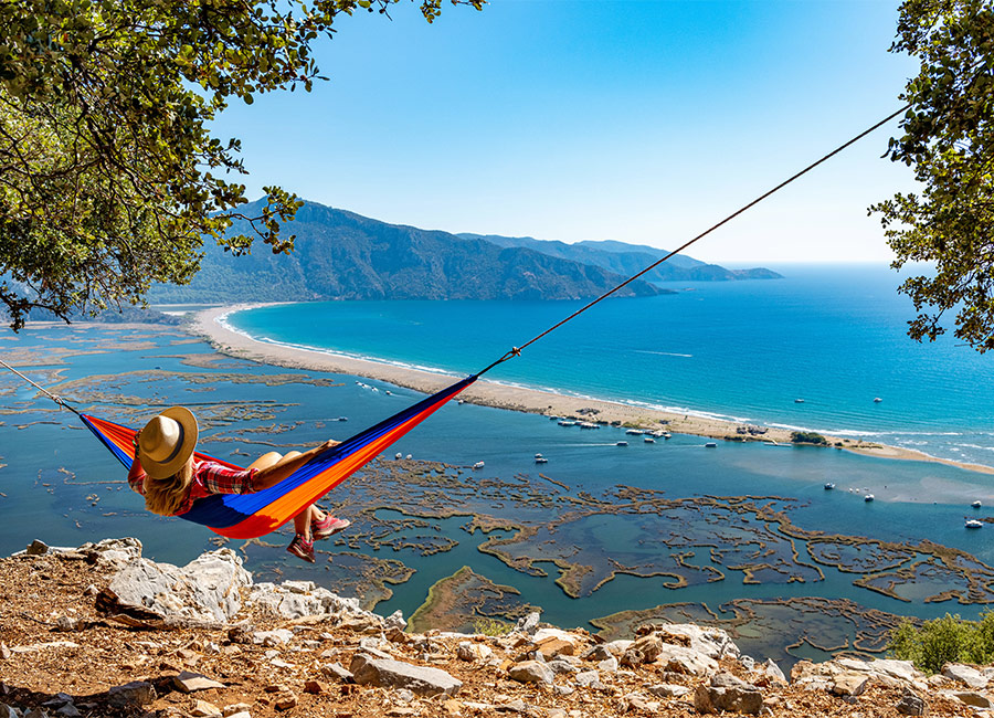 The woman lying in the hammock is looking at the beach with pleasure.