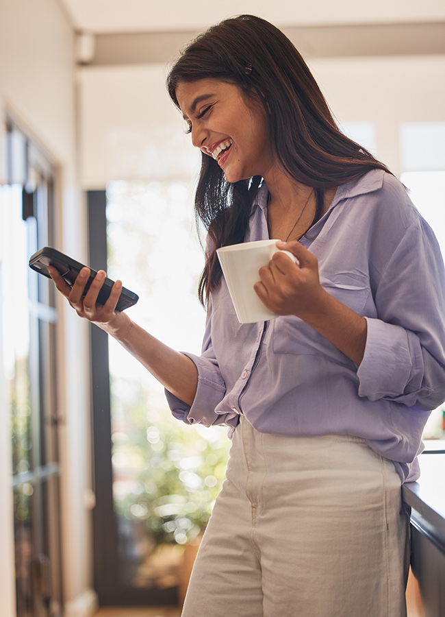 Happy woman, phone and coffee or tea at home while online for communication or social media and laughing at funny joke or meme. Female in her India house with smartphone for ecommerce or dating app