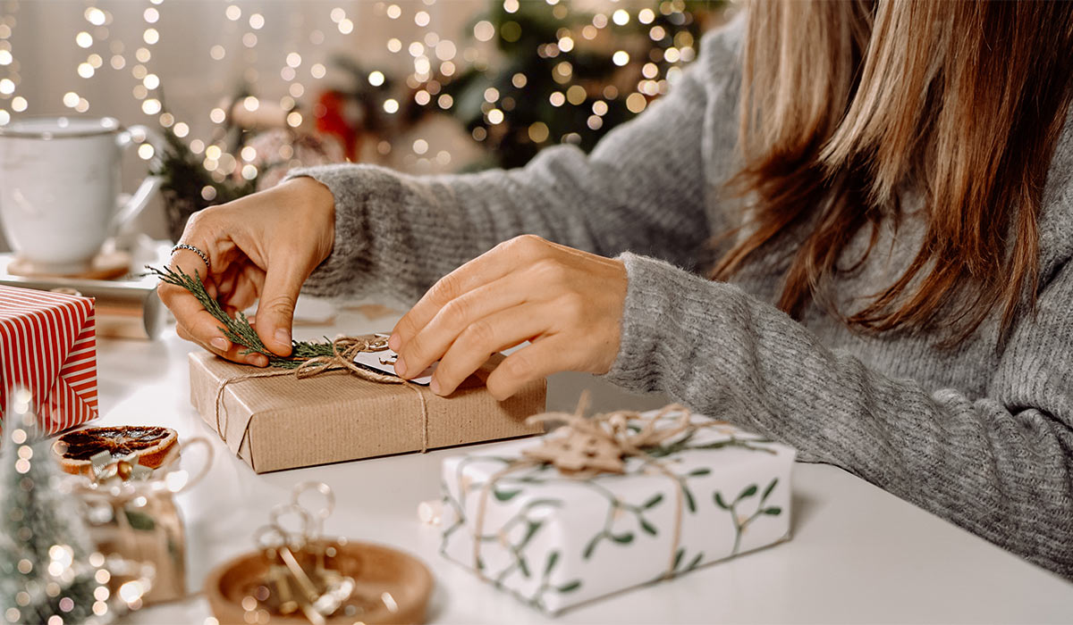 Woman s hands wrapping Christmas gift boxes, close up. Unprepared presents on white table with decor elements and items Christmas or New year DIY packing Concept.