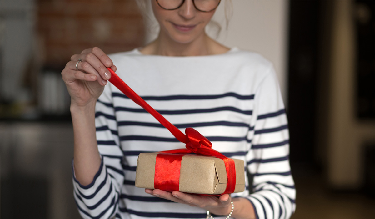Female hands holding gift box with red ribbon. Woman opening her present. Casual style.