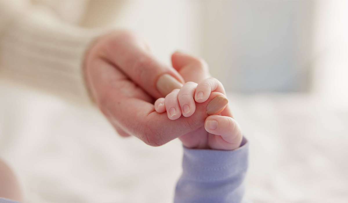 Sleeping, family and holding hands with baby on bed for bonding, love and relationship with infant. Adorable, care and closeup of parent with newborn for support, dreaming and protection at home