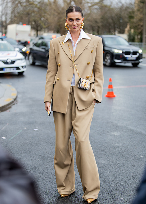 A guest wears beige double breasted oversized suit, blazer, pants, bag, white blouse, golden earrings outside Schiaparelli during Haute Couture Spring-Summer 2025 as part of Paris Fashion Week. Pic: Getty Images